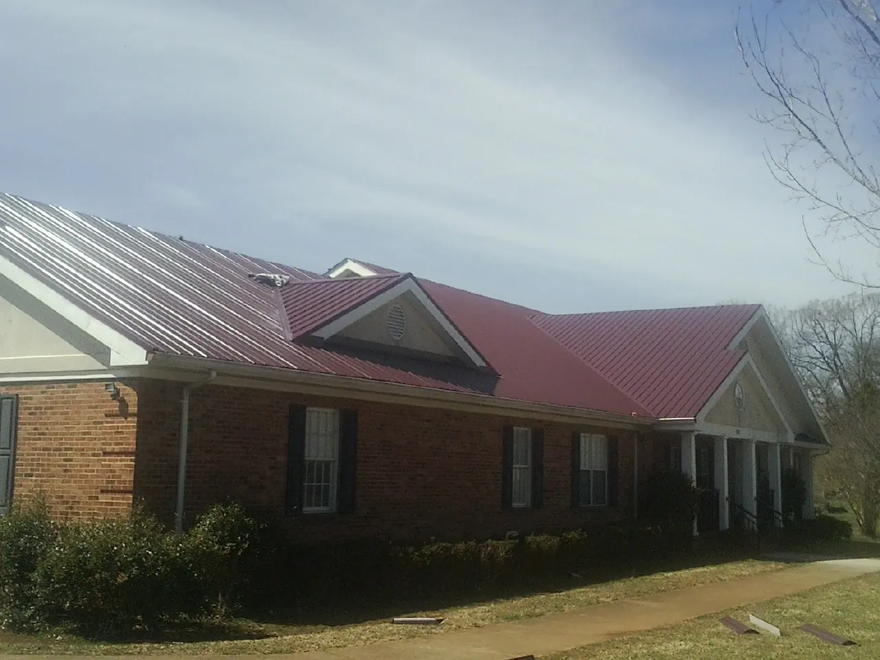 Red metal roof with gabled entries on a long brick building, from a Hail Damage Roof Repair job in Norristown