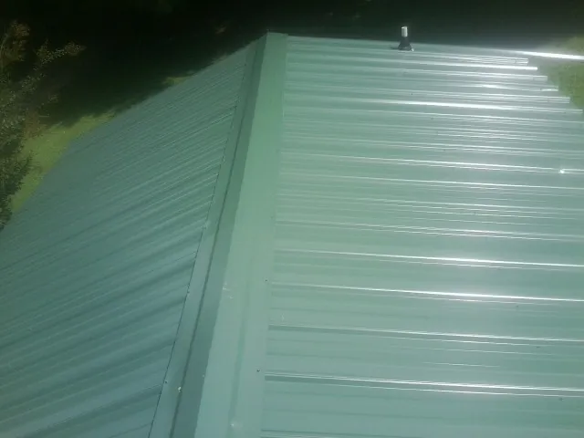 New green metal panels meeting at the ridge of a roof — Flat Roof Repair work by our crew in Norristown