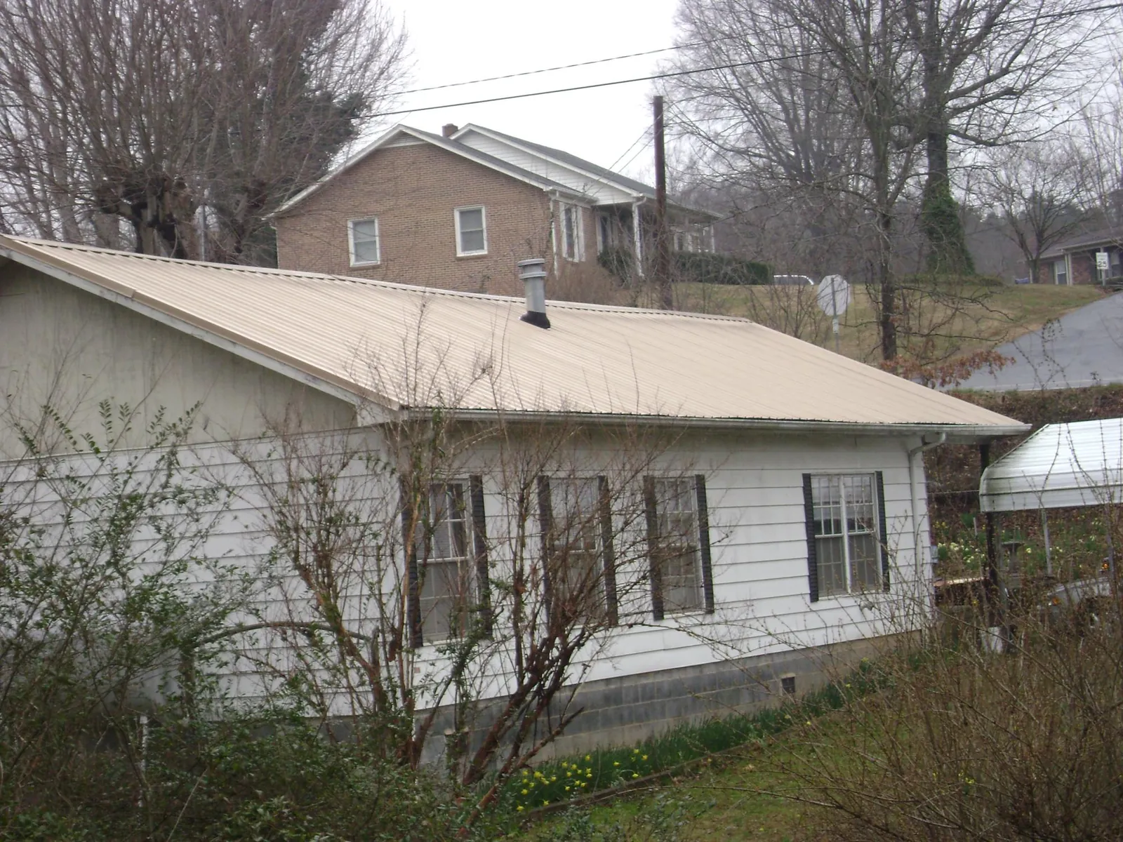 Tan metal roof on a white sided house set into a hillside — Commercial Roofing by Roofing Brothers in Norristown